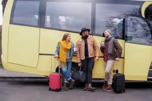 Amigos conversando ao lado de um ônibus amarelo, com malas e tomando um café, sobre os direitos de um viajante de ônibus.