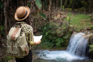 Mulher jovem com mapa na mão, olhando uma cachoeira que faz parte da rota de ecoturismo em São Paulo.