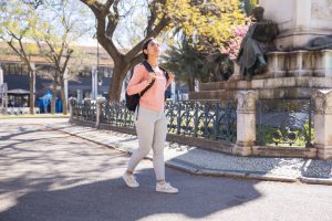 Mulher com mochila nas costas, andando em uma praça de Pindamonhangaba.