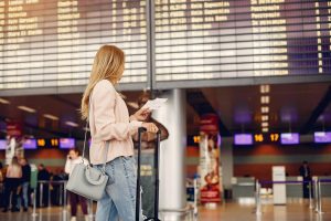 Menina jovem em pé após ter chegado da sua conexão no Aeroporto de Guarulhos, conferindo o status do voo com seu bilhete.